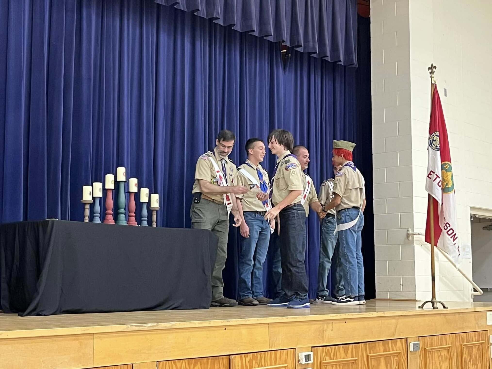 The scoutmaster giving an award to a scout.  He is joined by other adults and scouts standing beside him.