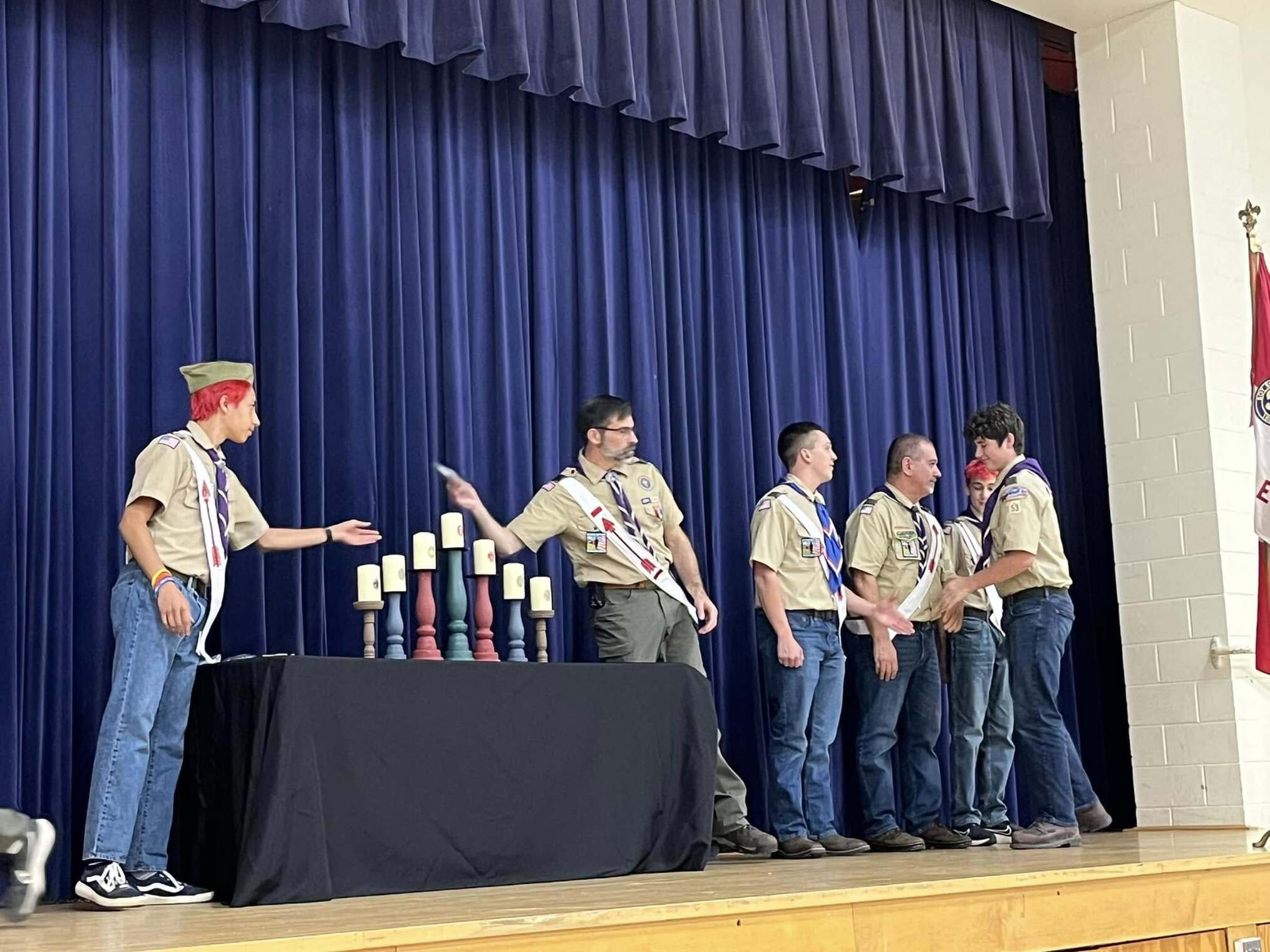 The scoutmaster giving an award to a scout.  He is joined by other adults and scouts standing beside him.