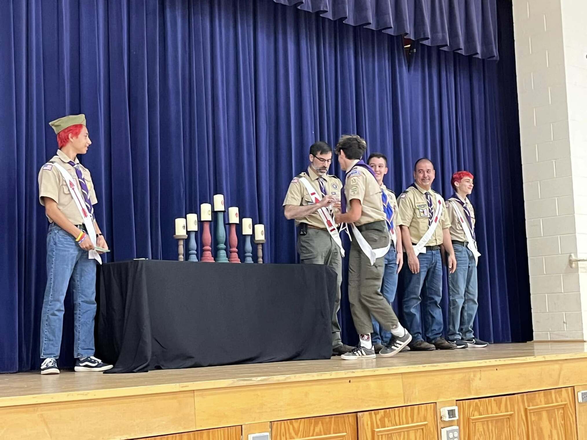 The scoutmaster giving an award to a scout.  He is joined by other adults and scouts standing beside him.