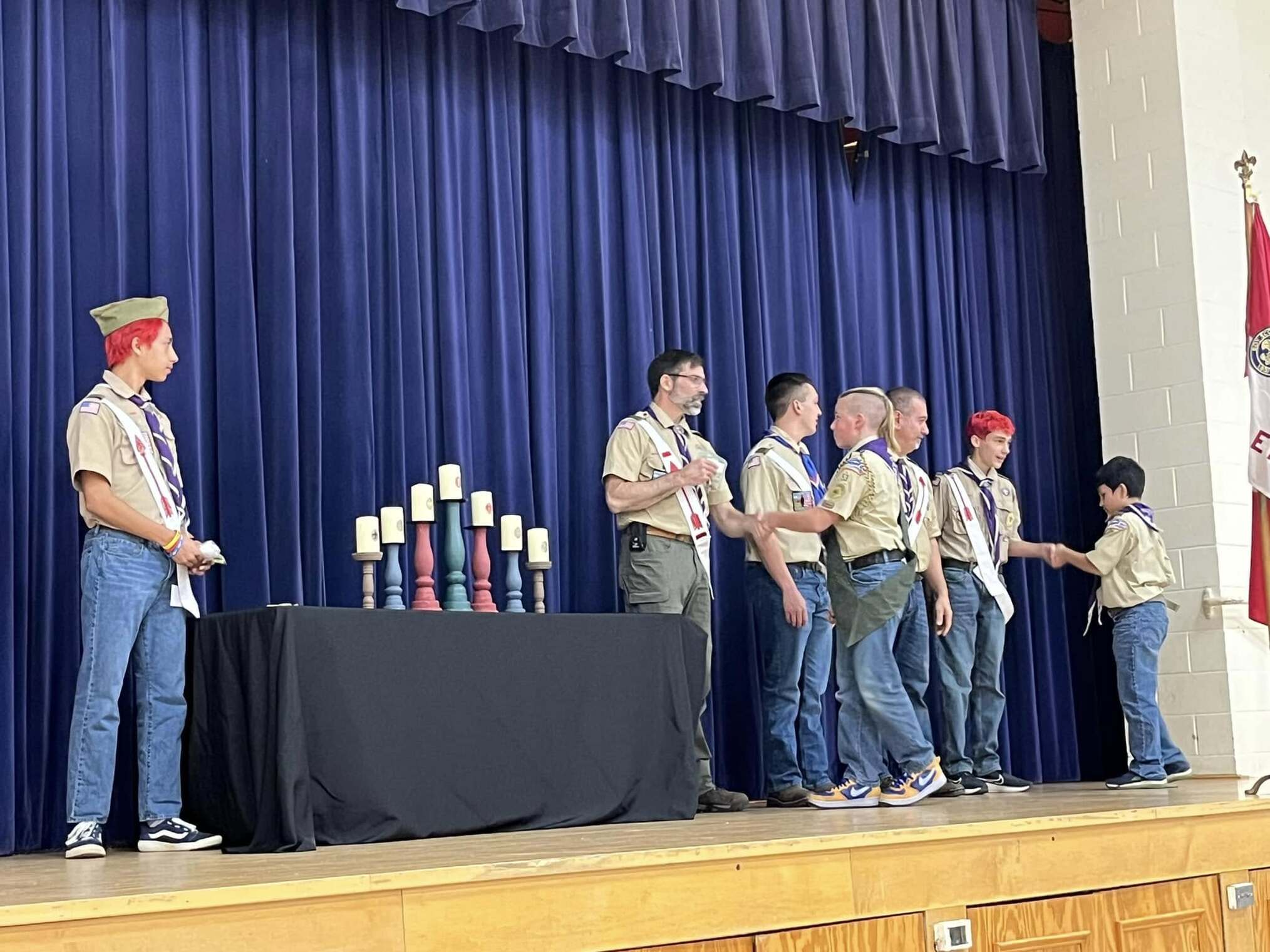 The scoutmaster giving an award to a scout.  He is joined by other adults and scouts standing beside him.