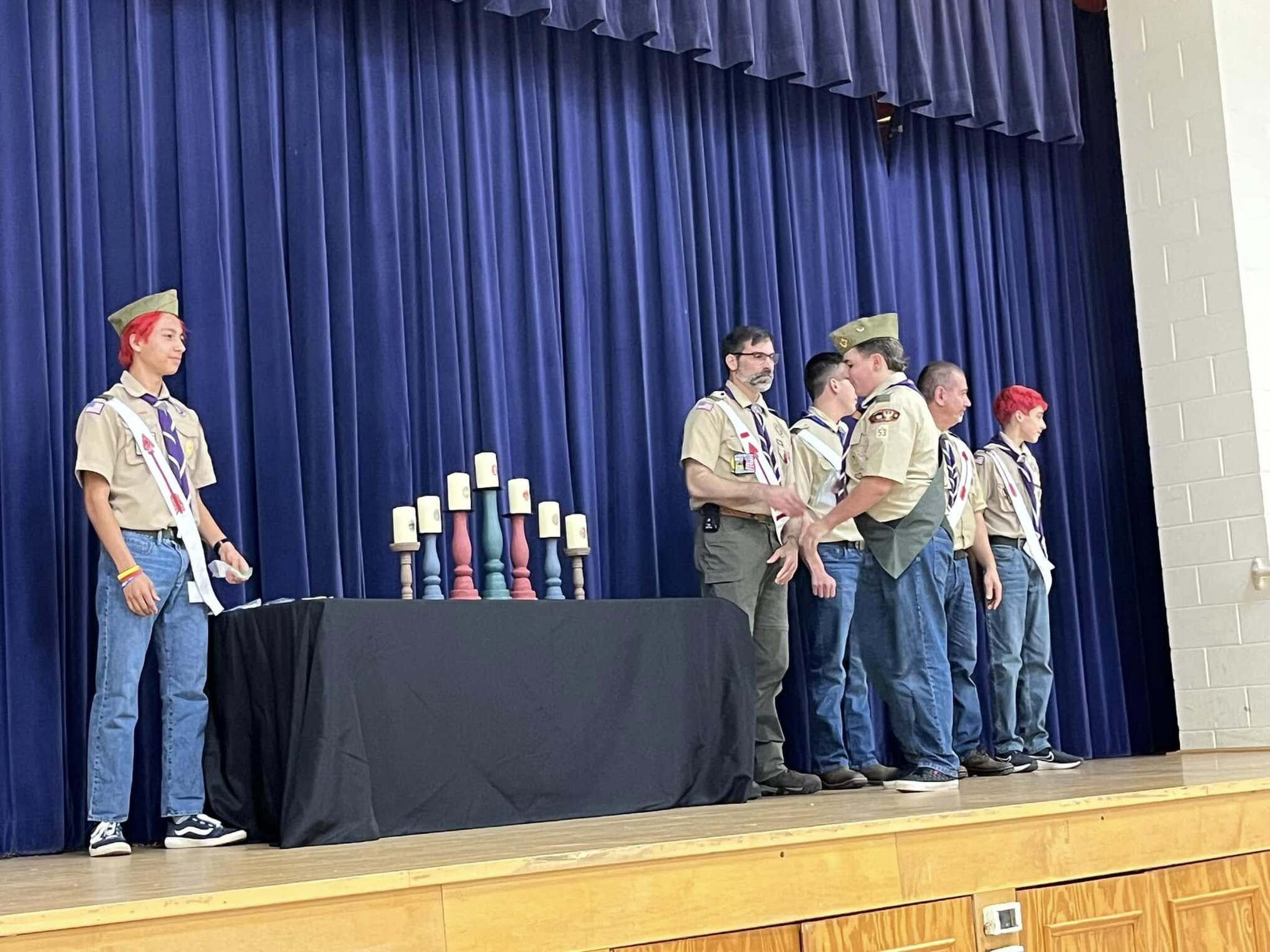 The scoutmaster giving an award to a scout.  He is joined by other adults and scouts standing beside him.