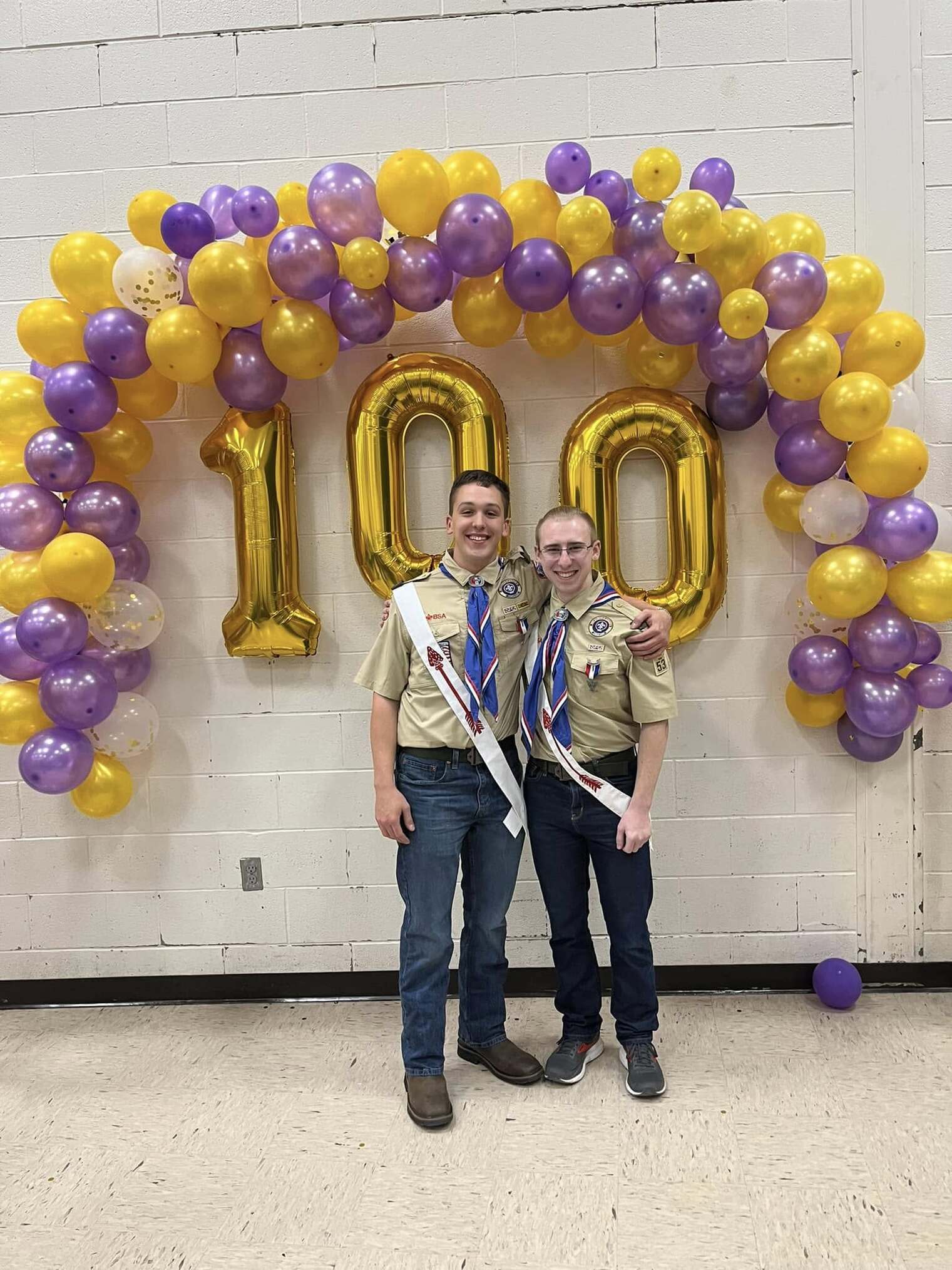 Two people in class A uniforms standing in front of a balloon wall with 