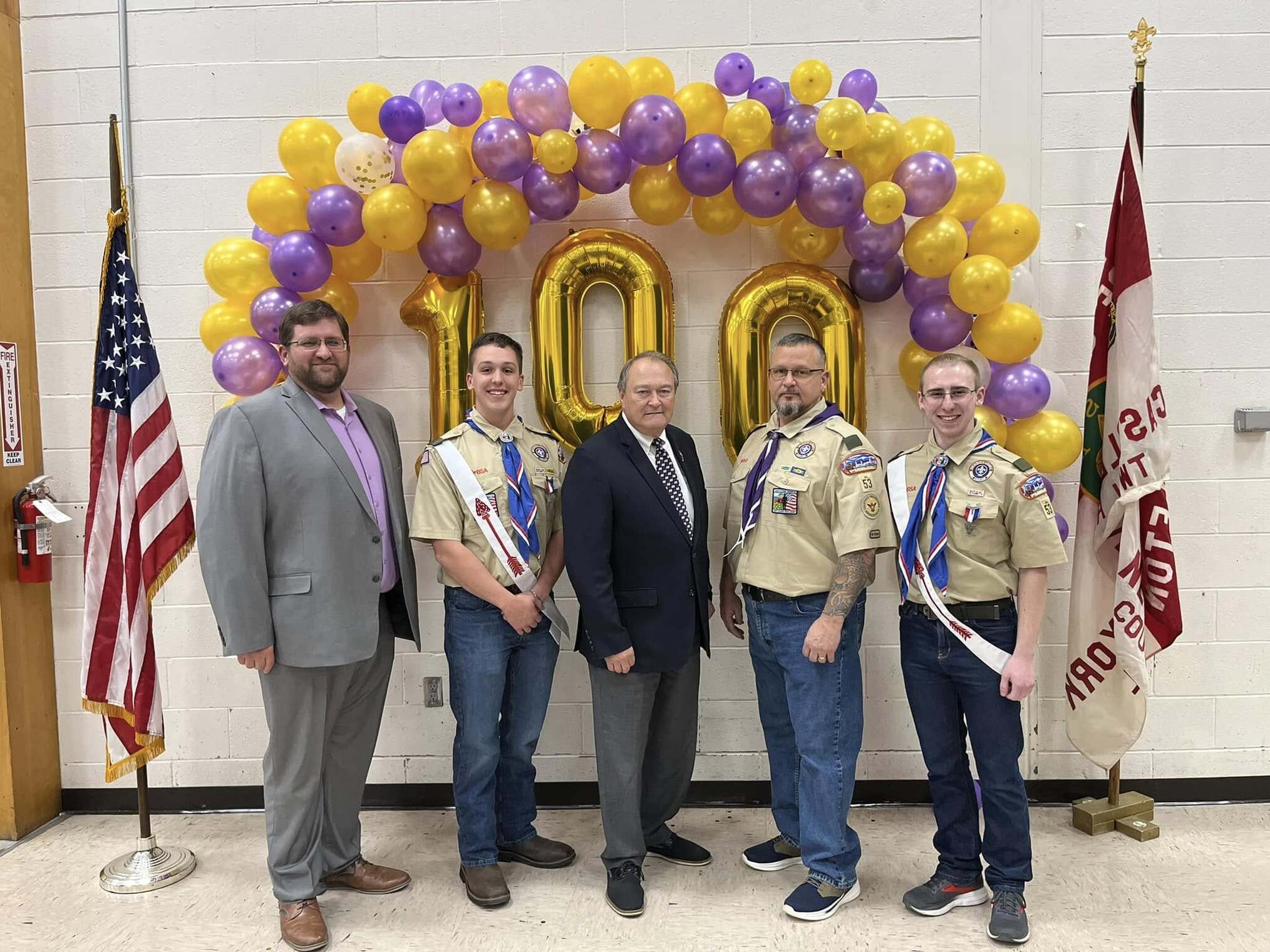 Three men in class A uniforms and 2 in suits stand in front of the balloon wall.